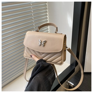 Detail of beige crossbody bag featuring V-shaped quilting and silver bow-knot buckle