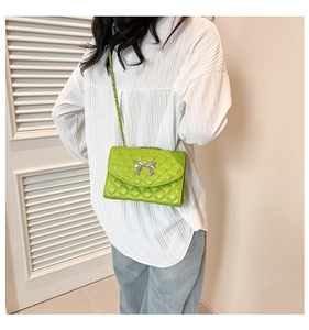 Détail d'un sac matelassé vert vif avec nœud argenté et chaîne porté par un mannequin