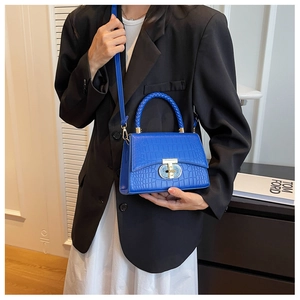 Close-up of bright blue crocodile pattern handbag featuring a woven handle and gold T-lock