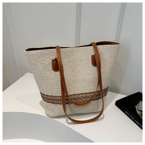 Detail of hand-woven straw tote bag with brown faux leather straps on a white desk