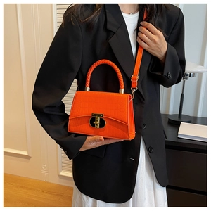 Detail of orange crocodile pattern handbag featuring a gold-tone clasp and woven handle