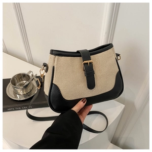 Detail of beige canvas crossbody bag featuring black leather trim and gold buckle accent