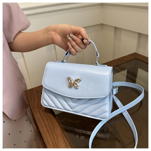 Close-up of light blue crossbody bag with butterfly buckle and V-shaped quilting detail