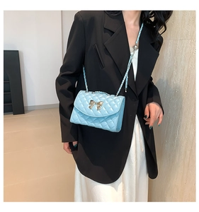 Gros plan du sac matelassé bleu clair avec boucle nœud doré porté par le mannequin