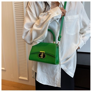 Detail of green crocodile texture handbag with golden T-lock and woven handle on model
