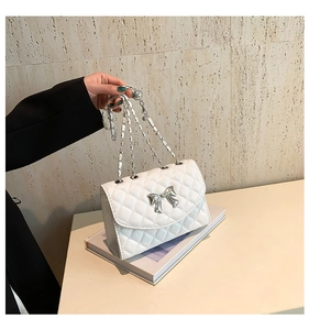 Détail du sac à bandoulière matelassé blanc avec nœud en métal argenté et bandoulière chaîne