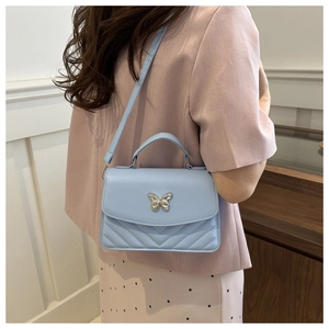 Detail of light blue crossbody bag with silver butterfly and V-quilted texture