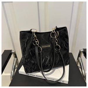 Dettaglio della borsa tote nera plissettata con manico a catena dorata e logo Fashion