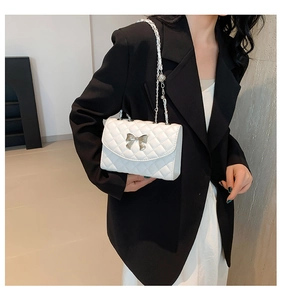 Close-up of white quilted leather texture with a silver metal bow on a fashion handbag