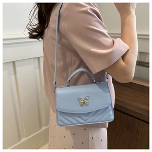 Detail of light blue crossbody bag featuring silver butterfly clasp and V-quilted texture