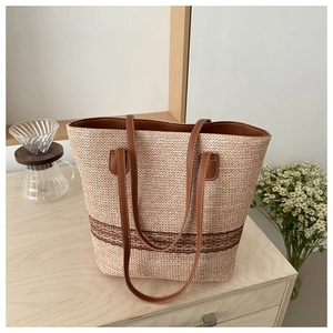 Detail of woven straw tote bag featuring brown leather handles and a striped base design