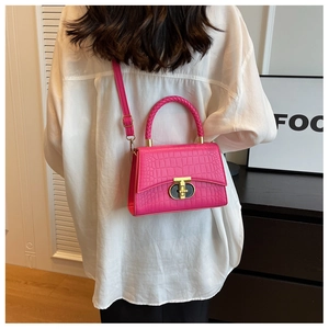 Detail of bright pink crocodile pattern handbag with golden twist lock and braided handle