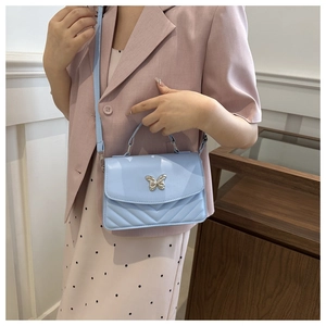 Detail of light blue quilted crossbody bag with decorative silver butterfly clasp