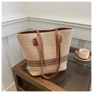Detail of beige woven tote bag with brown leather straps on a wooden table