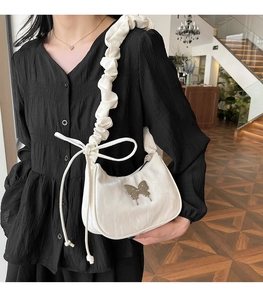 Detail of white underarm bag featuring butterfly metal ornament and ruched shoulder strap