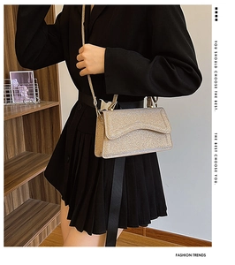 Detail of a golden sequin crossbody bag featuring a wavy flap design and shimmering finish