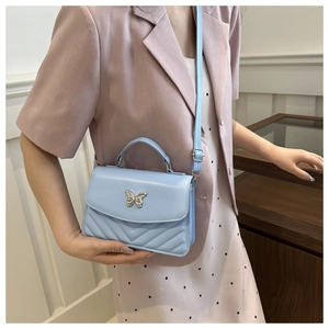 Detail of light blue crossbody bag with silver butterfly charm and V-quilt pattern