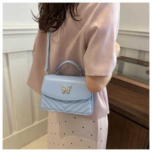 Close-up of light blue crossbody bag featuring a silver butterfly clasp and V-quilted texture