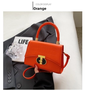Macro detail of orange crocodile pattern handbag with woven handle and gold clasp