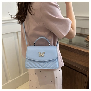 Detail of light blue quilted crossbody bag with silver butterfly buckle on a model