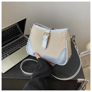 Detail of canvas crossbody bag with silver leather trim and golden buckle on a desk
