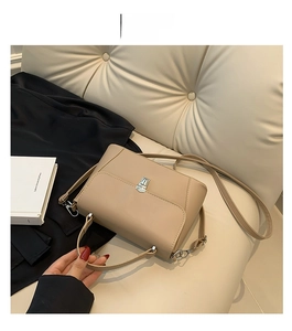 Detail of khaki leather handbag with silver twist lock and shoulder strap on sofa