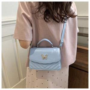 Close-up of a light blue quilted bag with a silver butterfly clasp worn by a model
