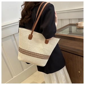 Close-up of cream woven straw tote bag with brown leather straps and floral embroidery