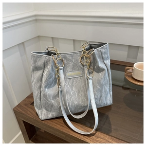 Dettaglio borsa tote a pieghe argento con catena dorata e marchio Fashion sulla scrivania