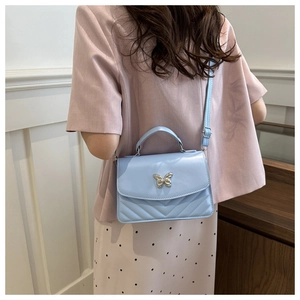 Detail of light blue quilted crossbody bag with metal butterfly clasp on a model