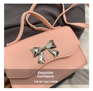 Close-up of pink crossbody bag featuring a textured leather finish and silver metal bow