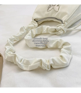 Detail of white pleated shoulder bag with long strap and silver butterfly ornament