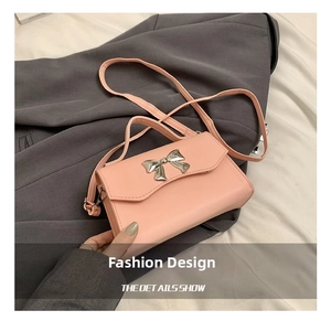 Detail of pink crossbody bag with silver metal bow and textured leather surface