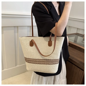 Shoulder view of straw tote bag with brown lace embroidery and leather straps
