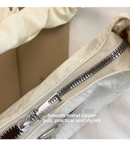 Close-up of silver metal zipper and pleated cream fabric detail on the shoulder bag