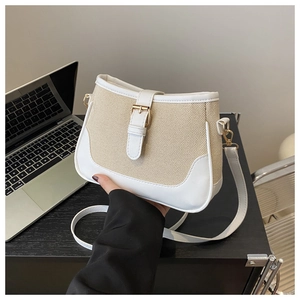 Detailed shot of white leather and woven canvas crossbody bag with gold buckle on a desk