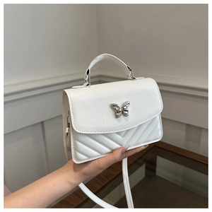 Detail of white quilted crossbody bag featuring a silver metal butterfly buckle and V-shaped stitching