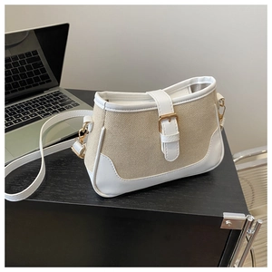 Detail of canvas and white leather patchwork crossbody bag with gold hardware on a desk