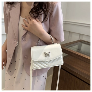 Close-up of white quilted crossbody bag featuring a silver butterfly clasp and V-shaped stitching