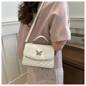 Close-up of white quilted crossbody bag featuring a silver butterfly buckle and top handle