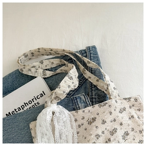 Close-up of floral tote bag with a white lace ribbon bow on a soft fabric background
