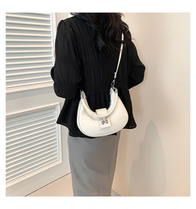 Sac demi-lune blanc avec boucle papillon argentée porté sur l'épaule par le modèle