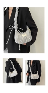 Detail of silver pleated crescent bag with metal butterfly and ruched shoulder strap
