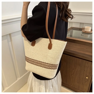 Detail of a beige woven straw tote bag featuring brown lace trim and leather straps