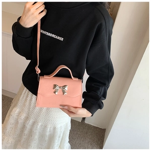 Detail of pink mini crossbody bag with silver bow buckle on textured leather finish