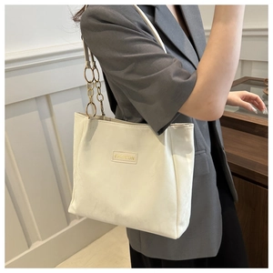 Dettaglio della borsa tote bianca con catena in metallo e patch FASHION mostrata sulla modella