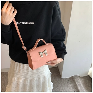 Close-up of pink crossbody bag with silver metal bow and adjustable shoulder strap