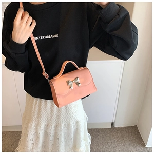 Detail of pink PU leather crossbody bag with silver bow buckle worn by a model