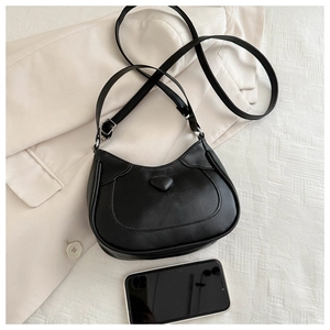 Detail of black semi-circle hobo bag with heart motif shown beside a phone for scale