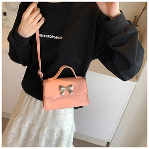 Detailed view of pink crossbody bag with silver metal bow and textured leather finish